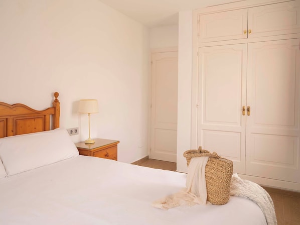 A bedroom with a wooden headboard, a bedside table with a lamp, a bed with white bedding, and a wardrobe with two doors. - Ona Aucanada Club (Alcúdia)