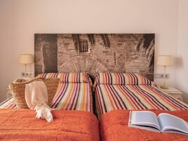 Habitación de hotel con dos camas, ropa de cama a rayas, un mural grande en la pared y un perro en la cama de la izquierda.