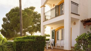 A two-story building with a balcony, a door with a green shutter, and a small table with chairs outside. - Ona Aucanada Club (Alcúdia)