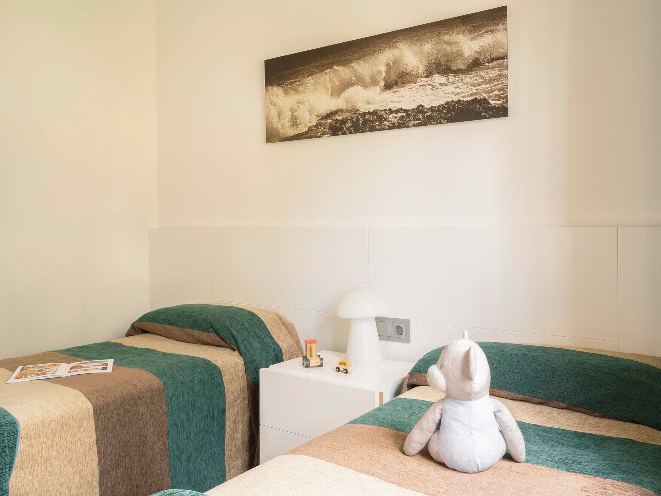 A room with two beds, a nightstand with a lamp, a plush toy, and a framed picture on the wall.