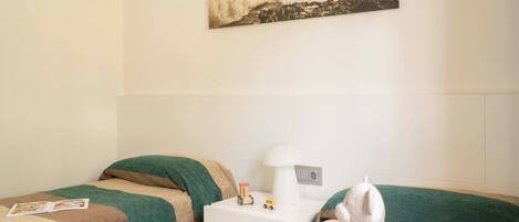 Une chambre avec deux lits, une table de chevet avec une lampe, un jouet en peluche et un tableau encadré au mur.
