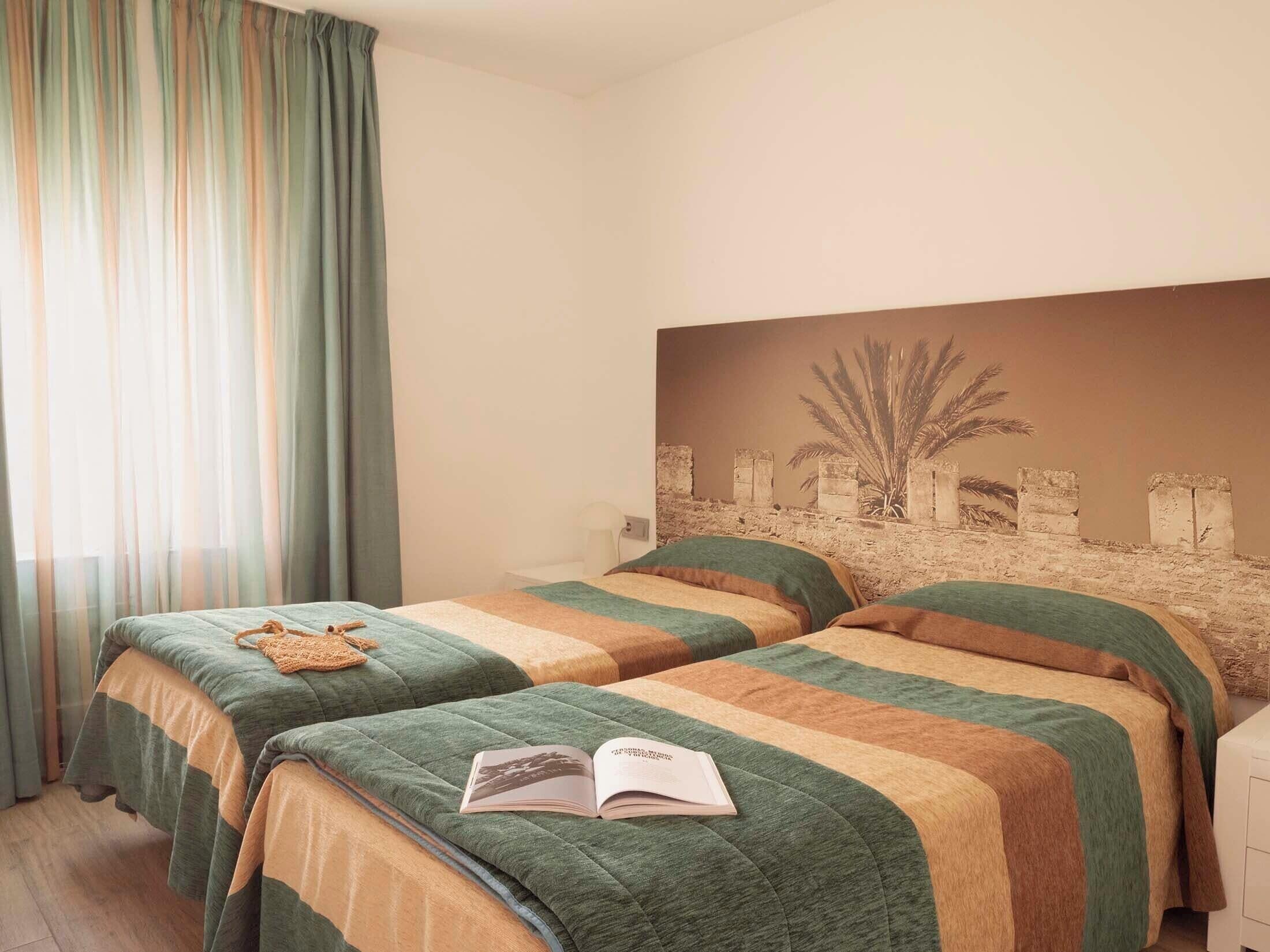 Habitación de hotel con dos camas, un ventanal con cortinas y una obra de arte colgada en la pared.