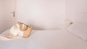 A bedroom with a bed, a white door, a nightstand with a lamp, and a woven bag on the bed. - Ona Aucanada Club (Alcúdia)