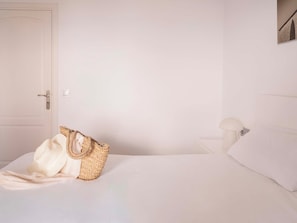 A bedroom with a bed, a white door, a nightstand with a lamp, and a woven bag on the bed. - Ona Aucanada Club (Alcúdia)
