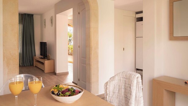 A modern room with a dining table, two glasses of orange juice, a bowl of fruit, a television, and a mirror on the wall. - Ona Aucanada Club (Alcúdia)