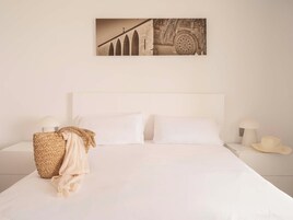 Un dormitorio con una cama grande, dos mesitas de noche, una cesta tejida y un cuadro colgado en la pared.
