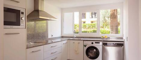 A modern kitchen with a built-in microwave, oven, and dishwasher, a window with a view of greenery, and a wooden floor.