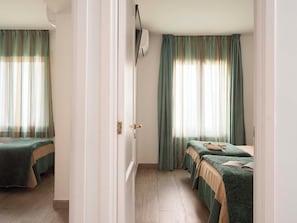 A hotel room with two beds, a wooden floor, and a window with curtains. - Ona Aucanada Club (Alcúdia)