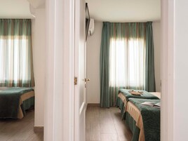 Habitación de hotel con dos camas, suelo de madera y ventana con cortinas.