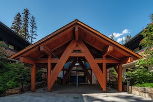 A wooden pavilion with a triangular roof structure, surrounded by greenery and trees.