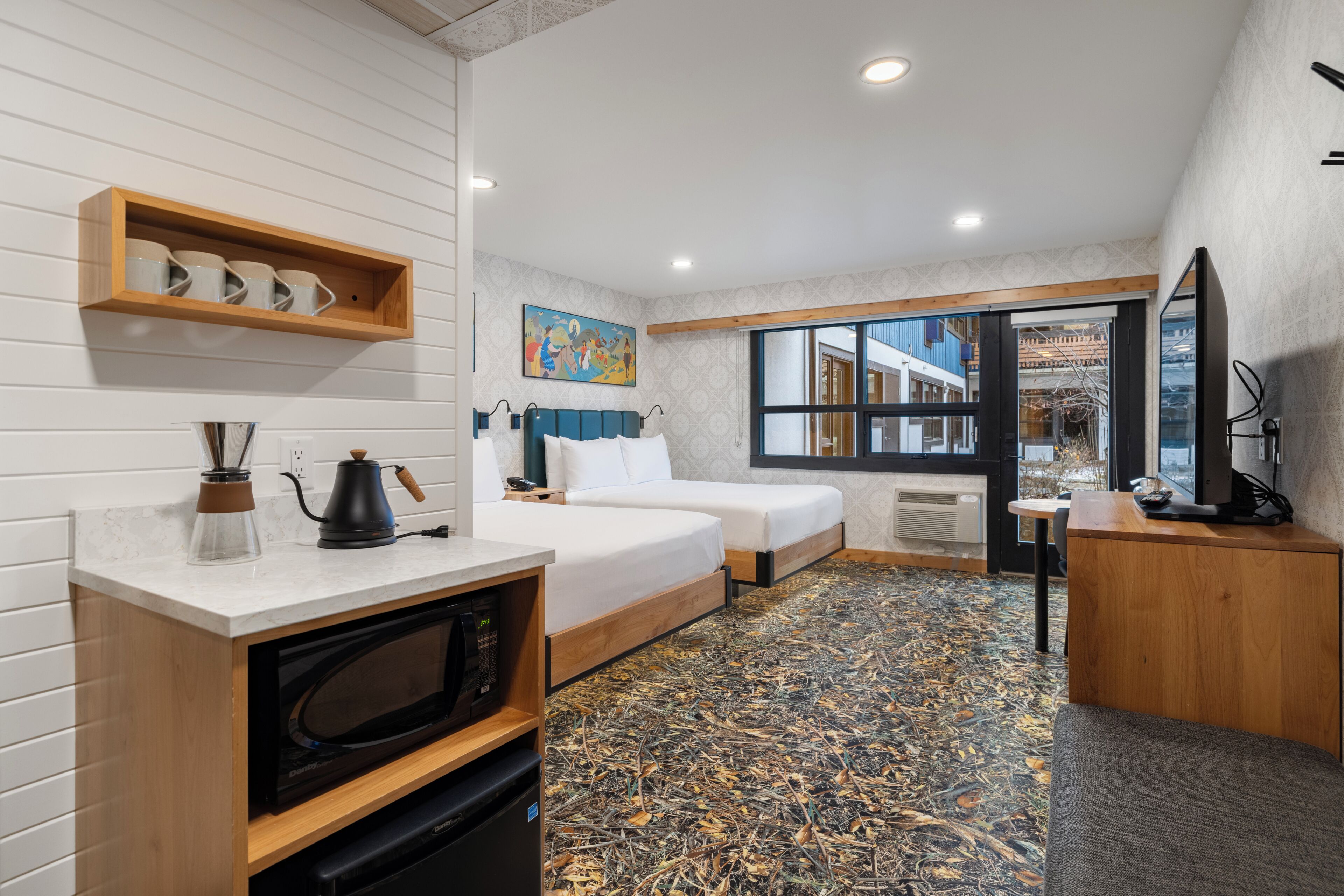 Une chambre d’hôtel compacte comprenant un coin cuisine, un lit, un bureau et une grande fenêtre donnant sur l’extérieur.