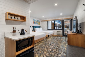 A compact hotel room with a kitchenette, a bed, a desk, and a large window offering a view of the outside. - The Dorothy Motel (Banff)
