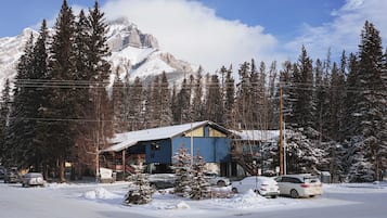 A mountain lodge with a snow-covered roof, surrounded by tall pine trees and a snow-covered mountain in the background.