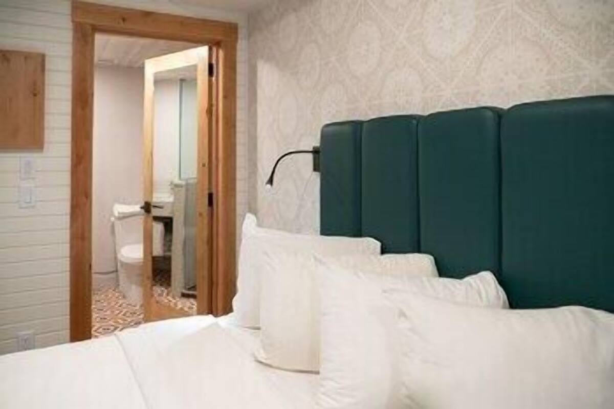 A room with a bed, a wooden door, and a bathroom visible through an open doorway.