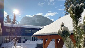 A snow-covered outdoor area with a wooden pergola, a building with large windows, and a mountain in the background.