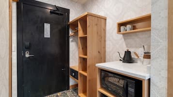 A compact kitchen with a black door, wooden shelves, a microwave, and a coffee maker.