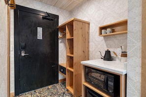 A compact kitchen with a black door, wooden shelves, a microwave, and a coffee maker. - The Dorothy Motel (Banff)