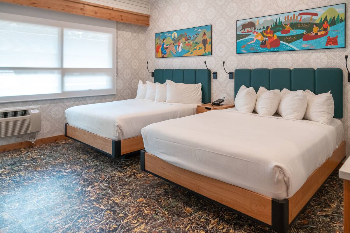 A hotel room with two beds, a large window, and two paintings on the wall.