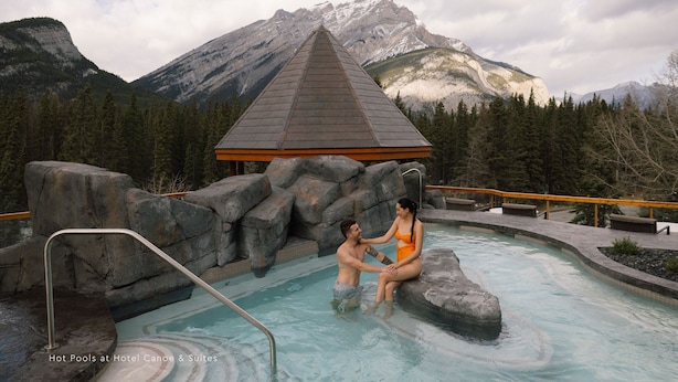 A hot pool area with a view of mountains, a wooden structure, and a rocky landscape.