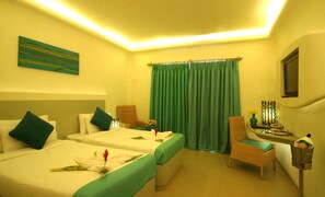 A hotel room with two beds, a green chair, a small table with a vase, and a wall-mounted TV. - The Golden Crown Hotel & Spa, Colva (Colva)