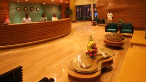 Una hall d'albergo moderna con una reception a forma di arco, zone relax e un tavolo decorativo al centro.