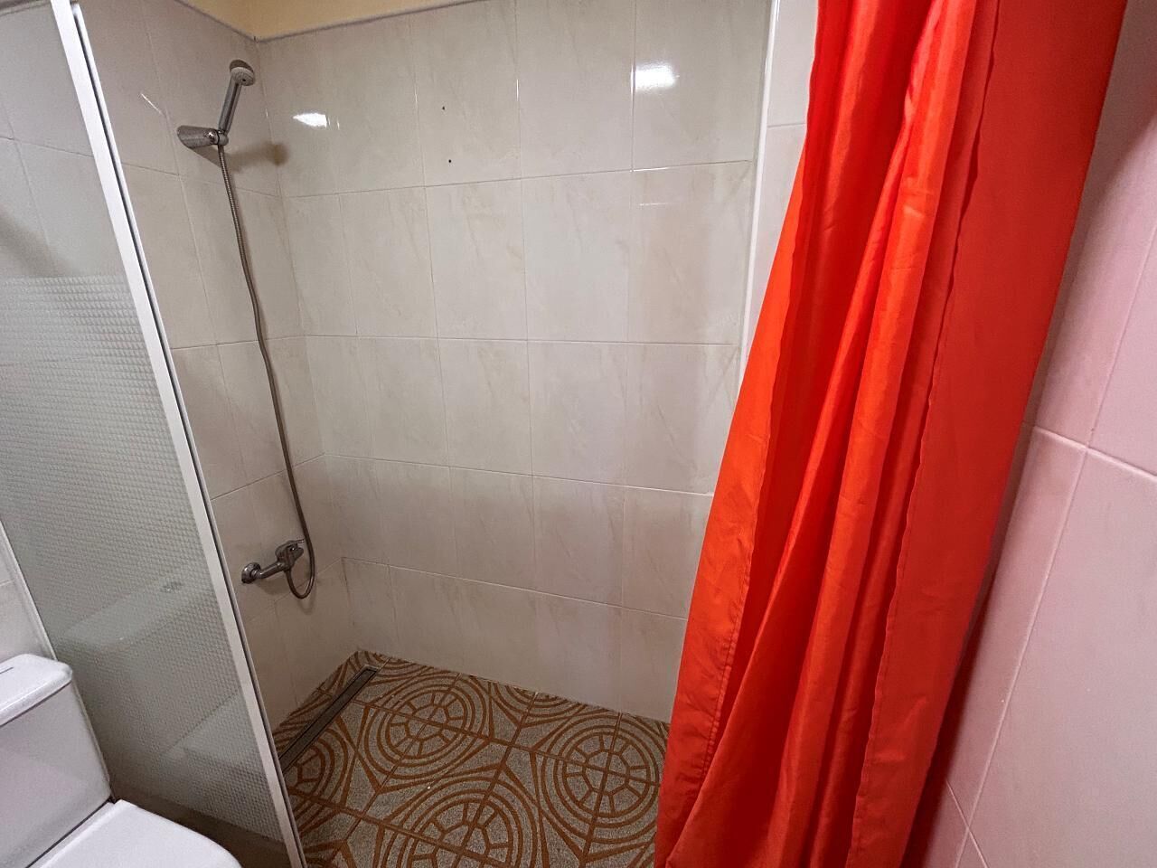 Ducha con puerta de vidrio, alcachofa y suelo con diseño.