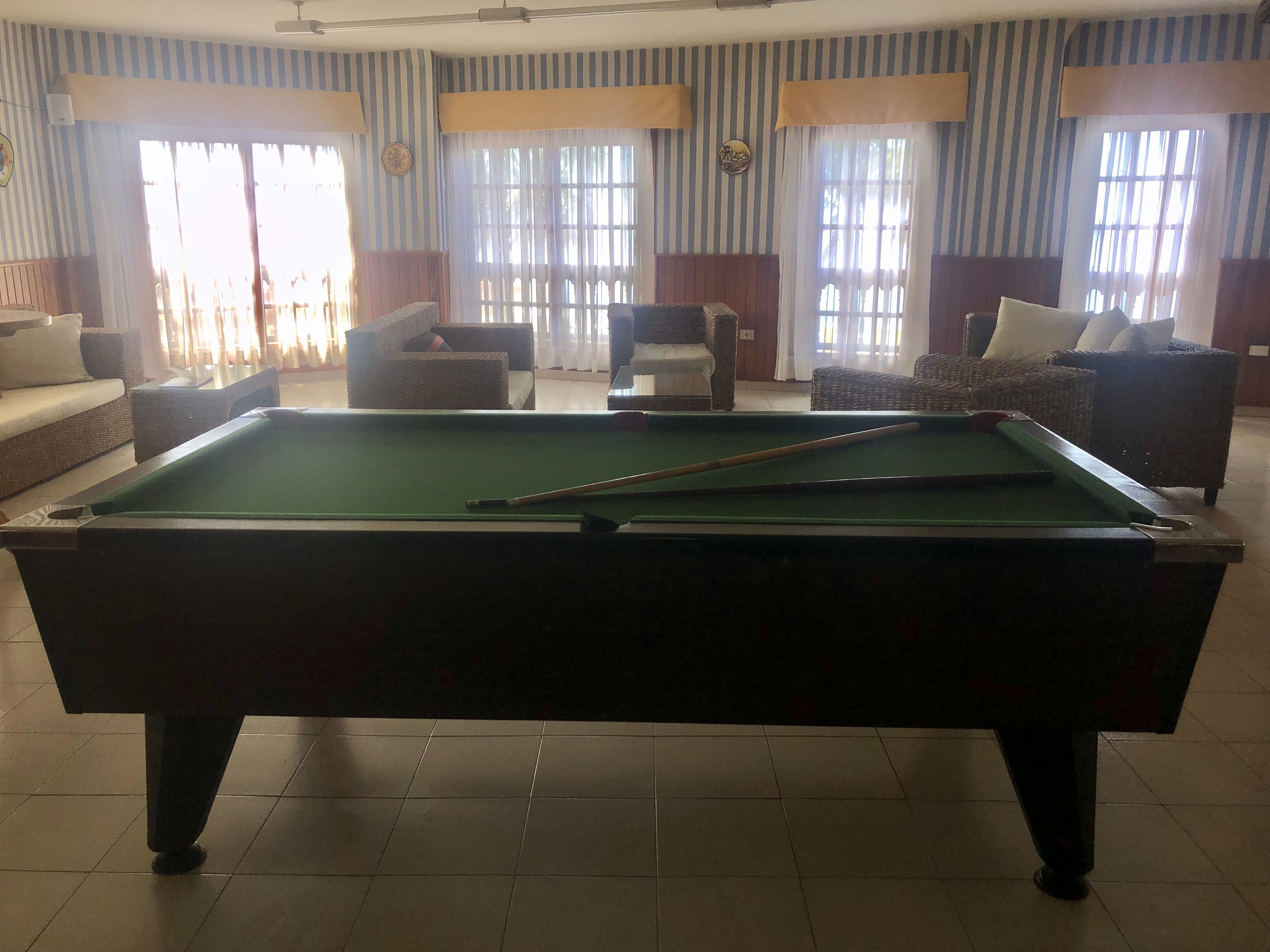A pool table in a room with striped wallpaper, a sofa, and a chair.