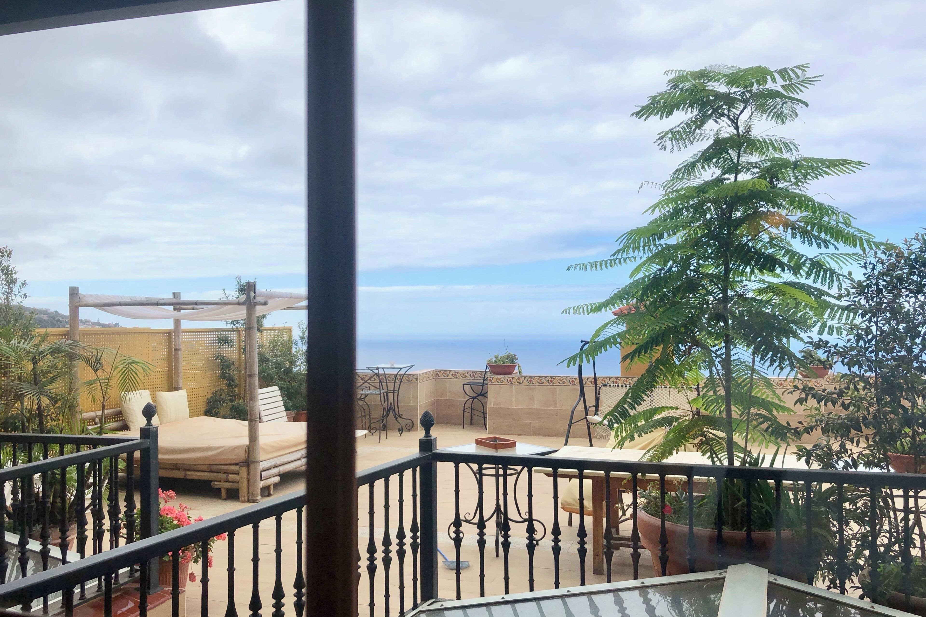 Un balcon aménagé avec un lit, un coin salon et des plantes en pot.