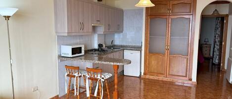 A kitchen with a dining area, wooden cabinets, a microwave, and a small refrigerator.