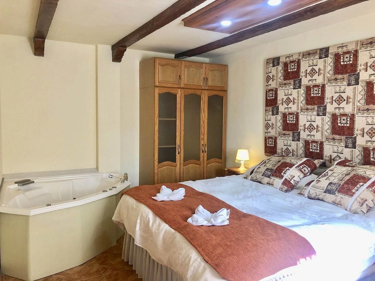 A bedroom with a bed, a wooden wardrobe, a bathroom with a bathtub, and a patterned wall.