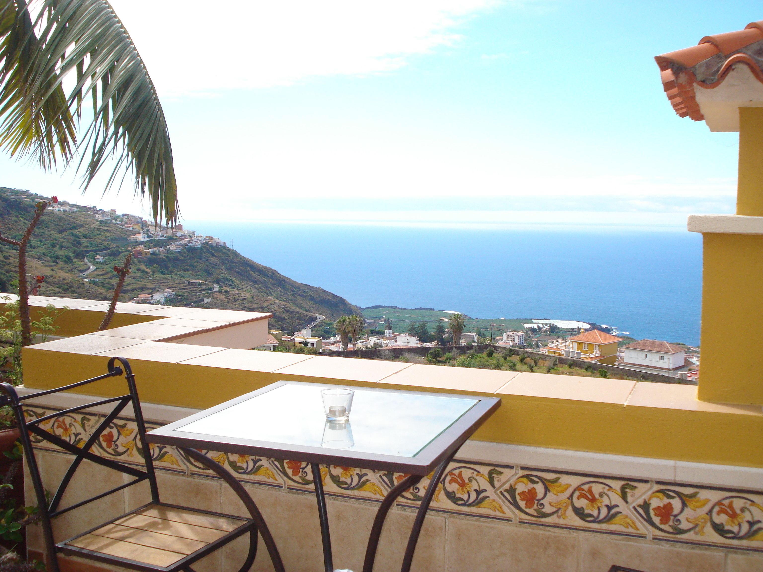 A balcony with a table and chairs overlooking a coastal view.