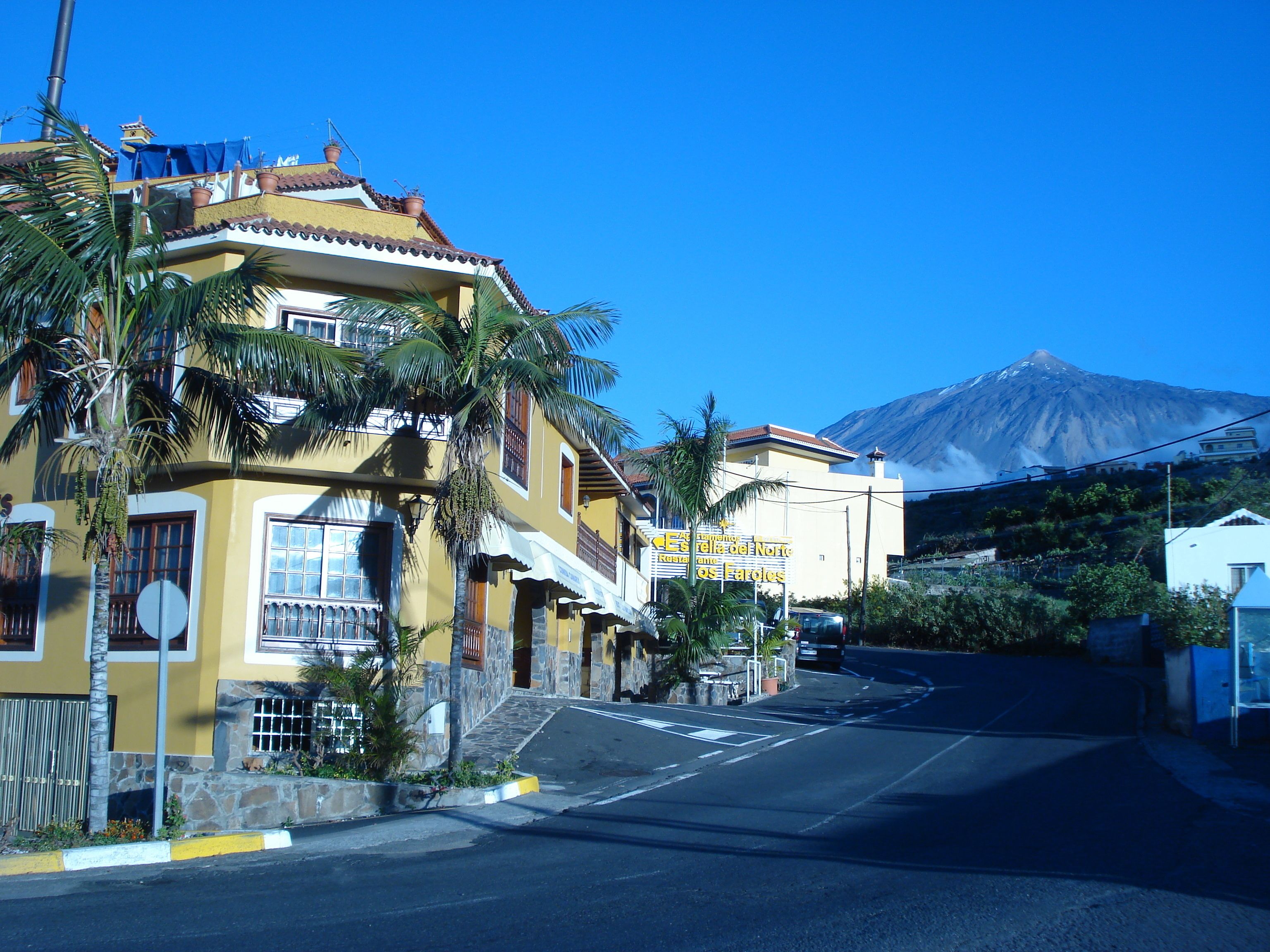 A yellow building with a balcony, a mountain in the background, and a clear sky.