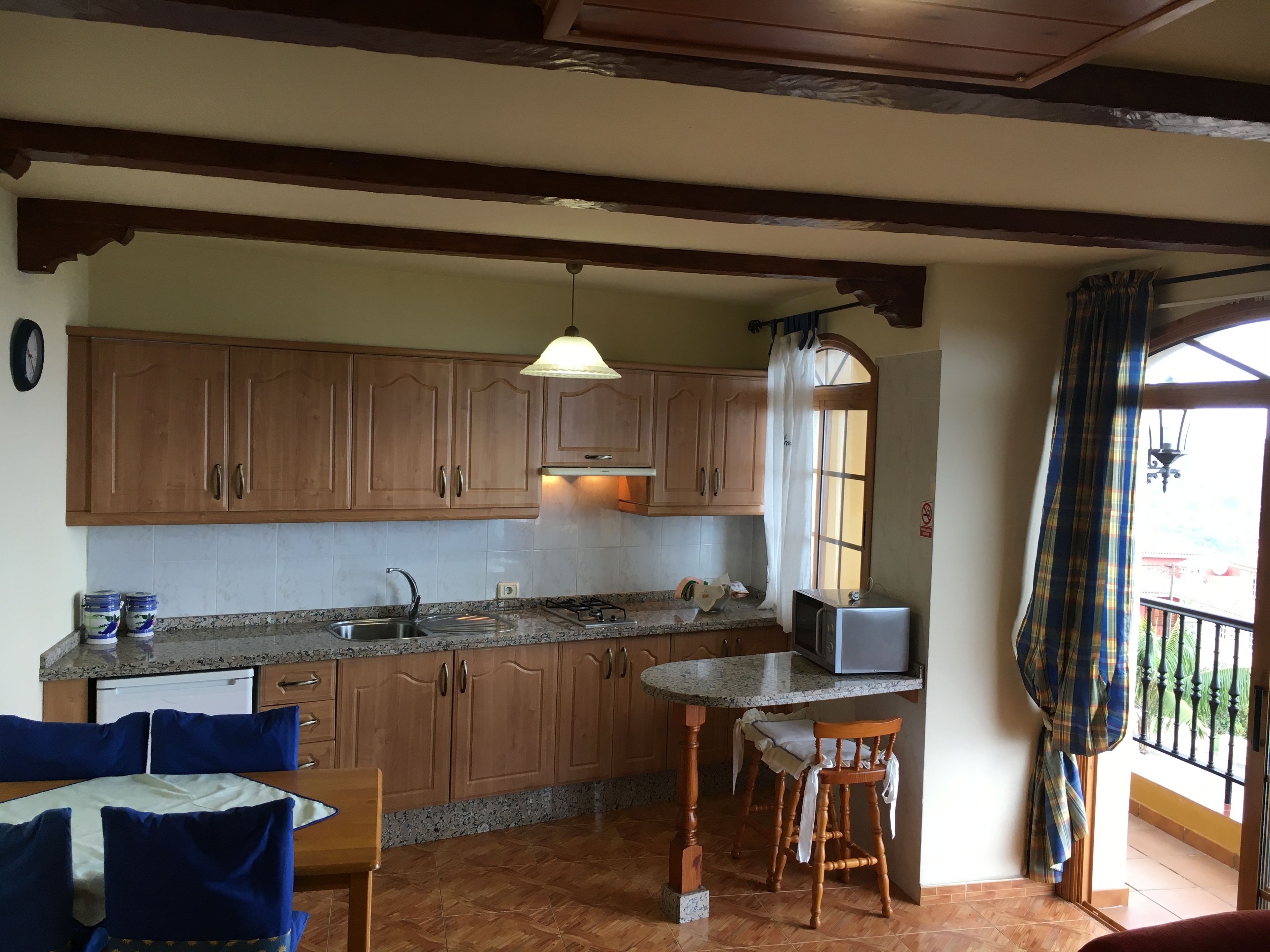 A kitchen with wooden cabinets, a granite countertop, a sink, a gas stove, a microwave, and a dining area with a table and chairs.