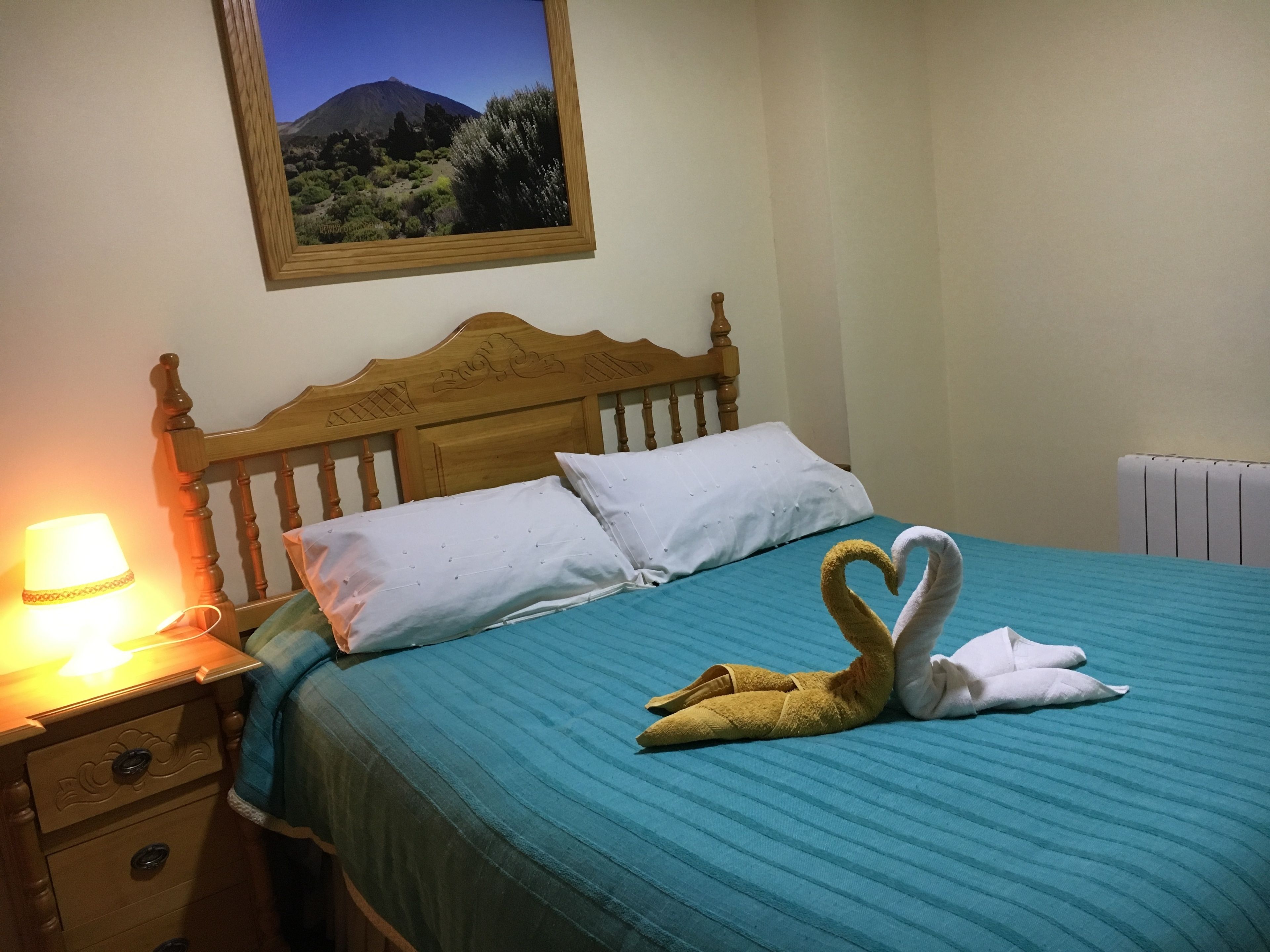 A neatly made bed with a blue bedspread, two pillows, and a swan-shaped towel arrangement.