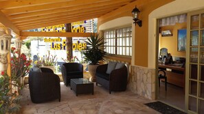 Relax in a serene outdoor space with wicker furniture, a large potted plant, and a wooden pergola.