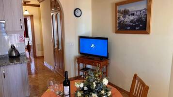 Un coin repas avec une table dressée pour deux personnes, un téléviseur et une horloge au mur.