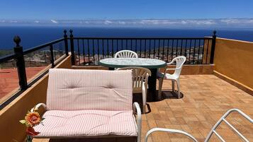 Uma varanda com vista para o oceano, uma mesa e duas cadeiras.