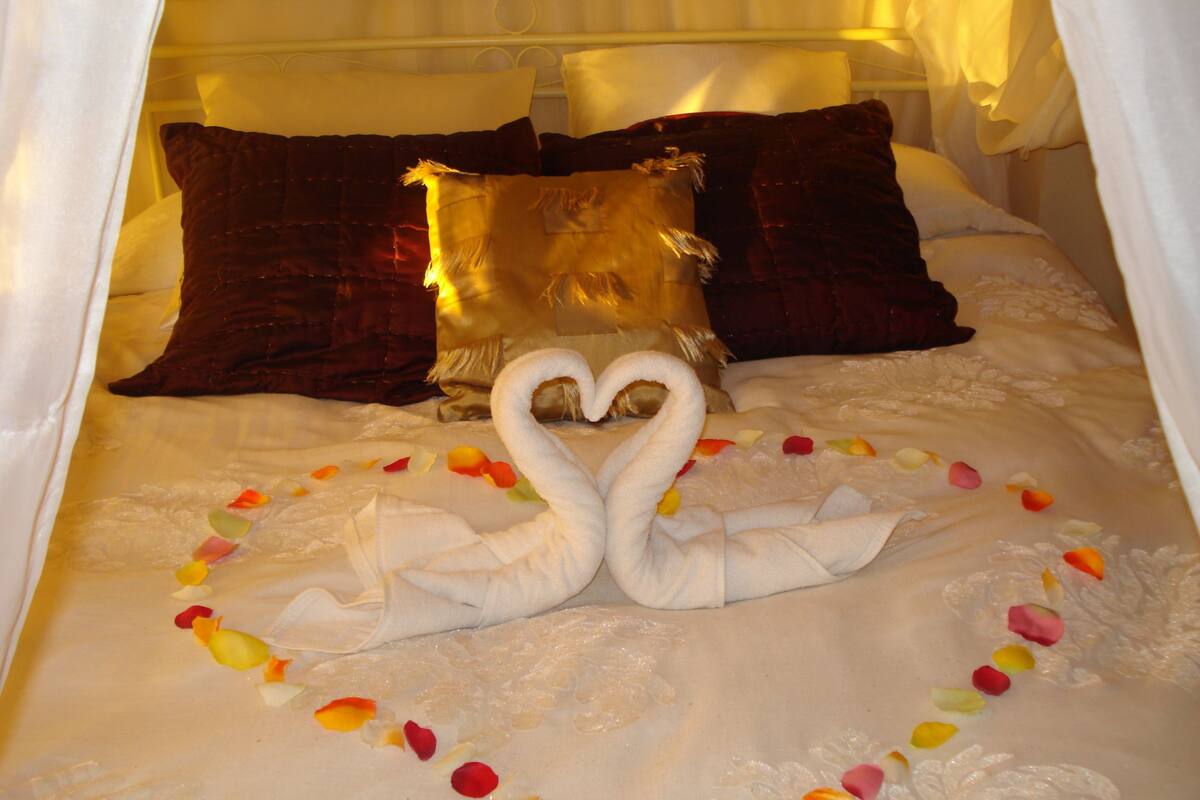 A bed with a swan-shaped pillow arrangement and rose petals.