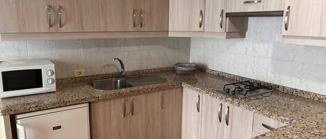 Une cuisine avec des meubles de couleur bois clair, un plan de travail en granit, un four à micro-ondes encastré, un évier et une cuisinière.