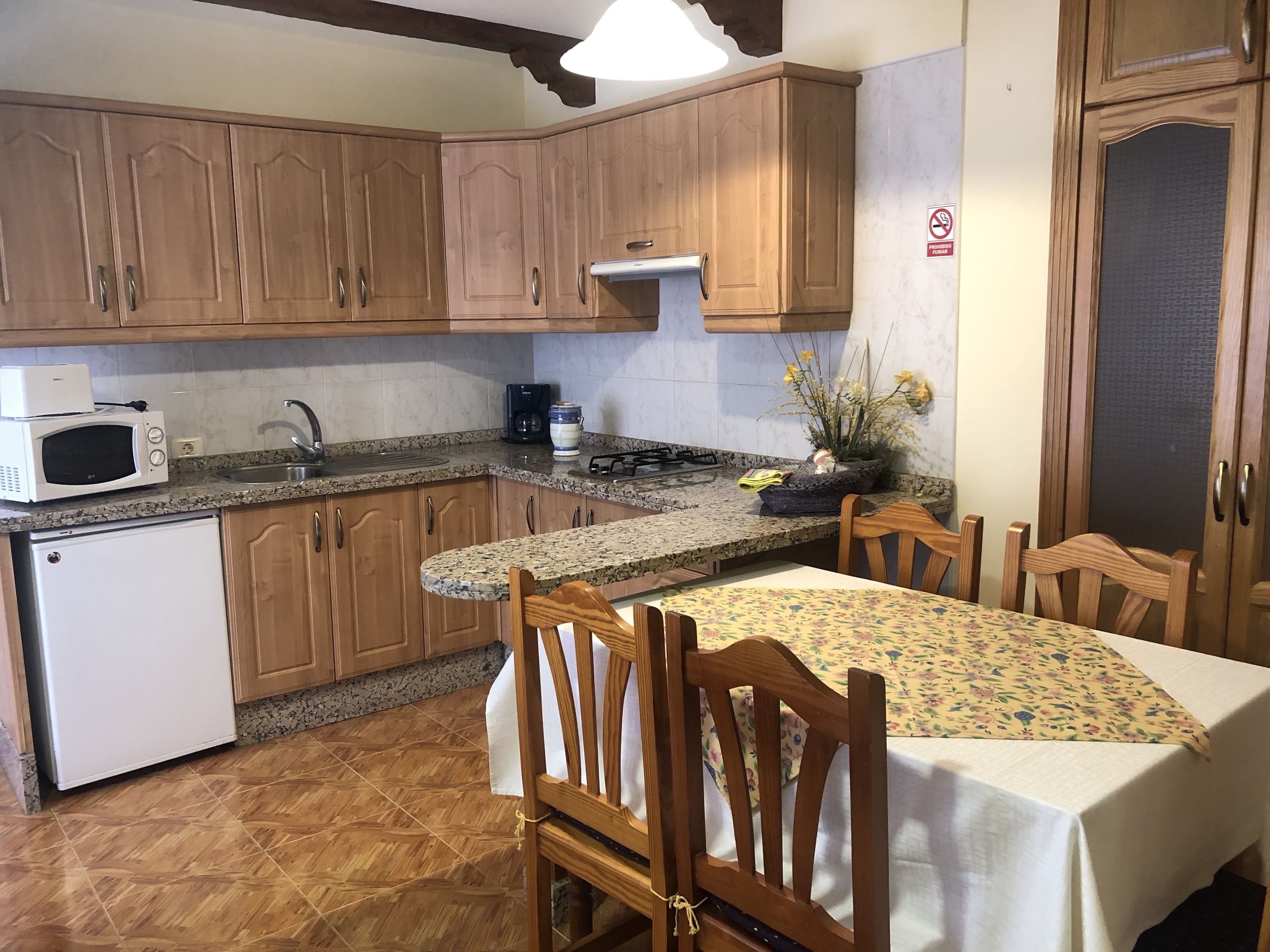 Una cocina con armarios de madera, microondas, fregadero y una mesa de comedor con sillas.