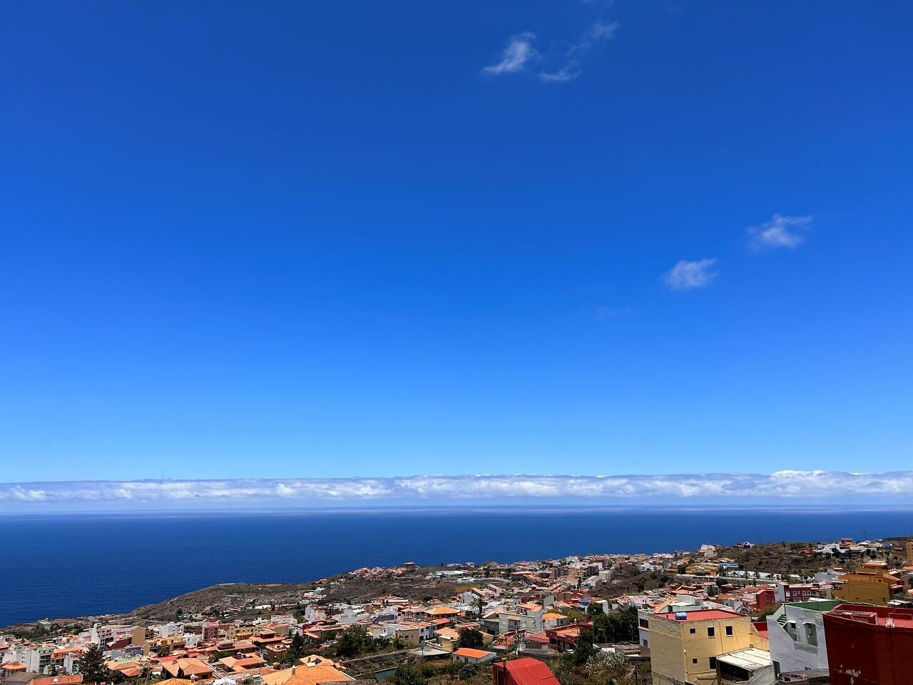 Un poble costaner amb edificis i vistes al mar i a les muntanyes a la distància.