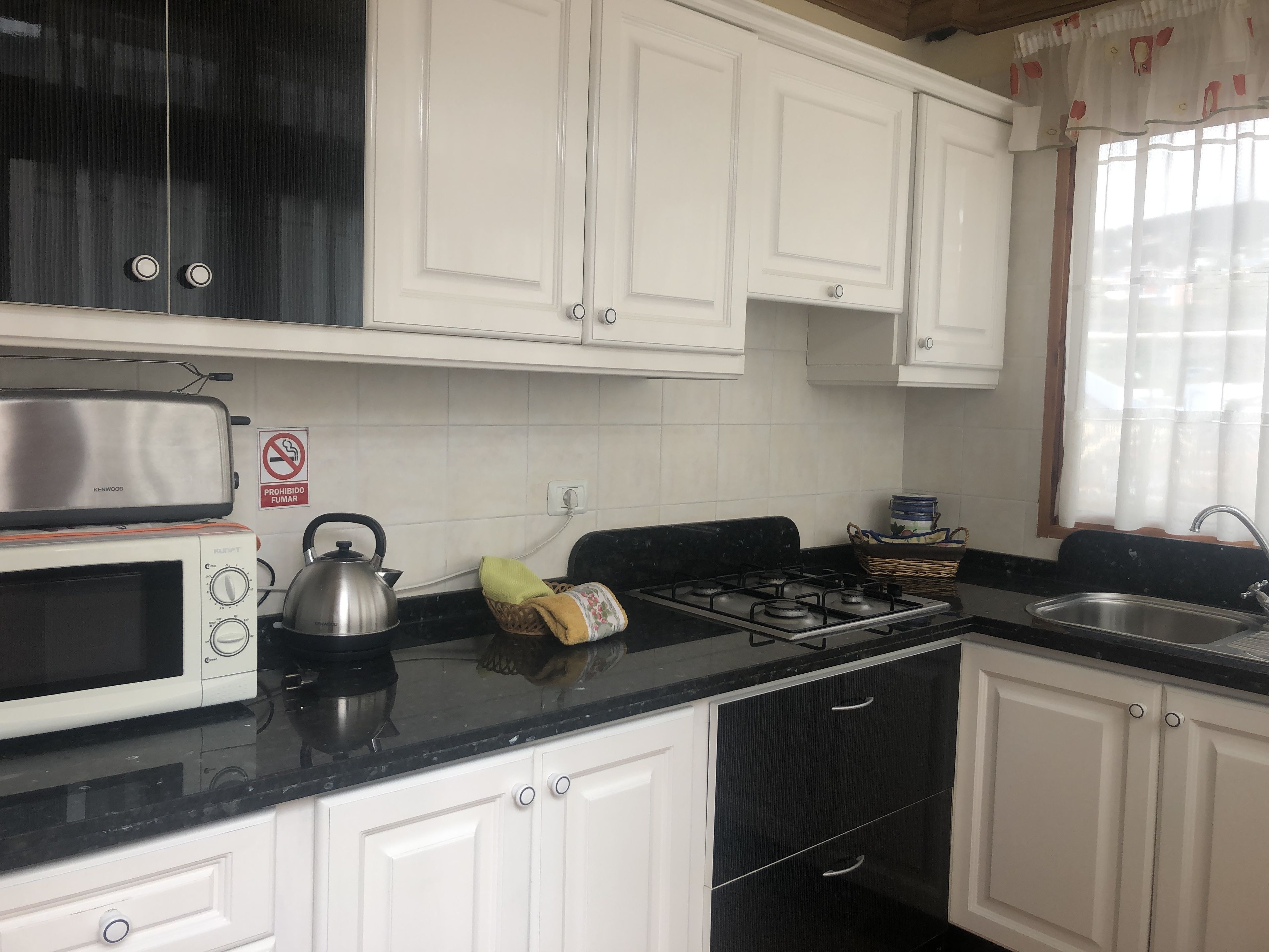 Cucina con mobili bianchi, un piano di lavoro nero, un fornello, un bollitore, un forno a microonde e un lavello.