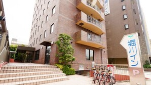 Un immeuble à plusieurs étages, doté d’une façade en briques, d’un escalier menant à l’entrée et d’un panneau indiquant un espace de stationnement.