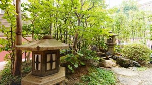 Un jardin japonais traditionnel, avec des lanternes en pierre, un jardin de rochers et une végétation luxuriante.