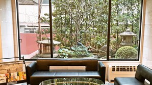 Un intérieur moderne avec une table basse en verre, des canapés en cuir et une vue sur un jardin agrémenté d’une lanterne en pierre.