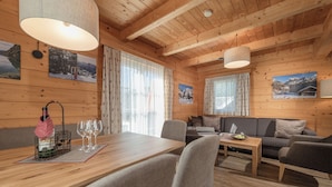 A cozy cabin interior with a wooden dining table, gray sofa, and a wooden ceiling with exposed beams. - AlpenParks Hagan Lodge Altaussee (Altaussee)