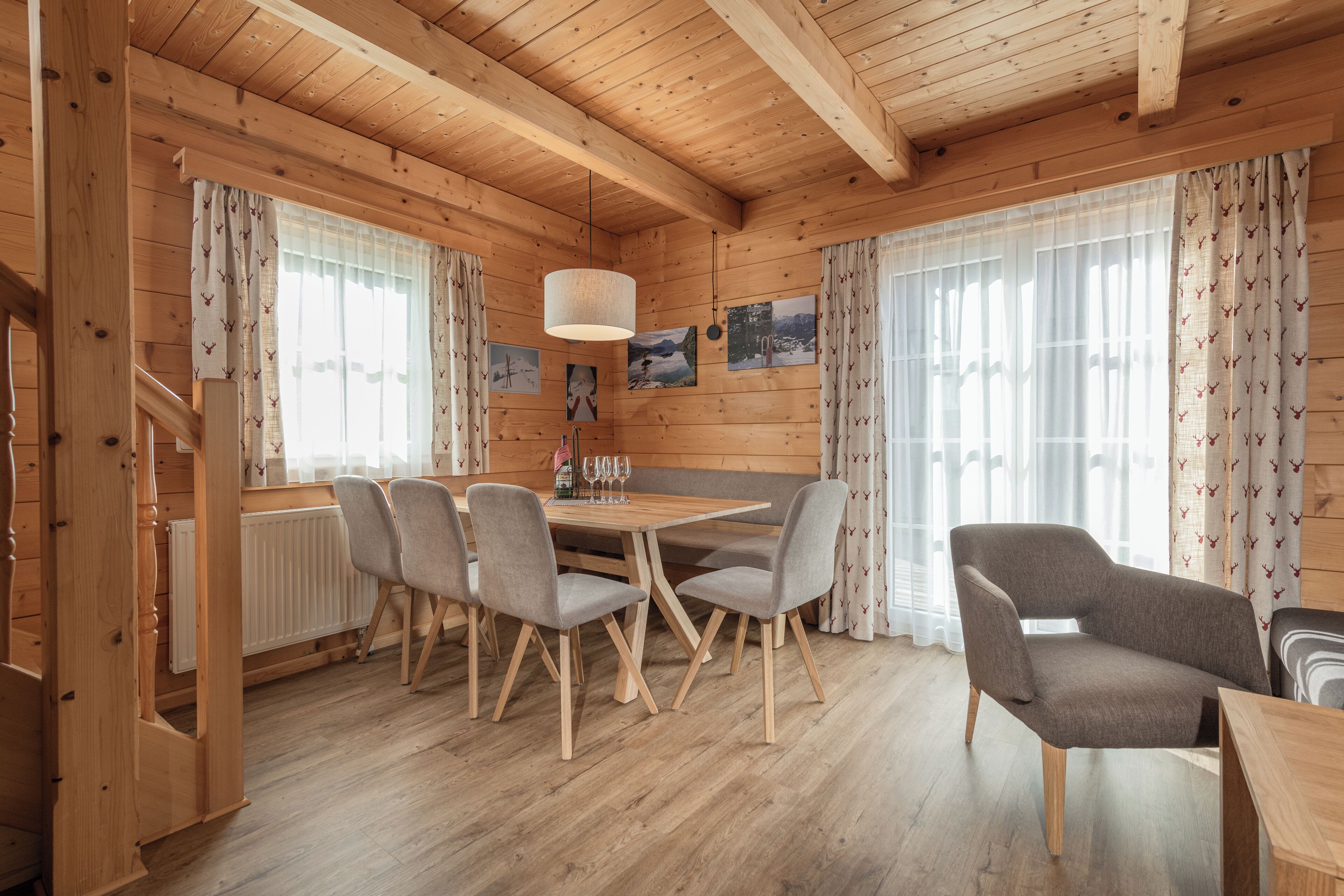 A wooden cabin interior with a dining table, chairs, and a bench.