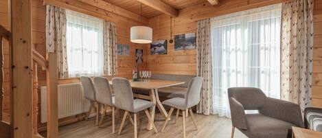 A wooden cabin interior with a dining table, chairs, and a bench.