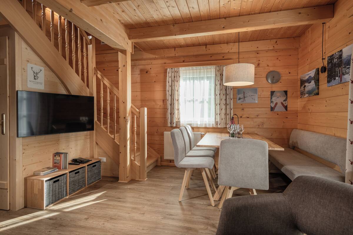 L’intérieur d’un chalet en bois comprend un coin repas, un canapé, un téléviseur et un escalier.