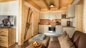 A cozy cabin interior with a wooden ceiling, a kitchenette, a sofa, and a television. - AlpenParks Hagan Lodge Altaussee (Altaussee)